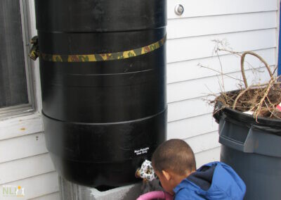 child filling watering can from rain barrel
