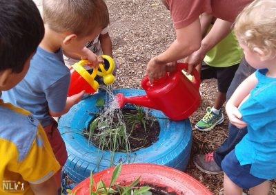 adult showing children how to water plants in tire planters